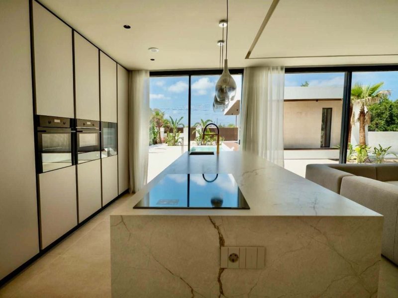 Kitchen with a long stone island and built-in ovens along a fitted wall