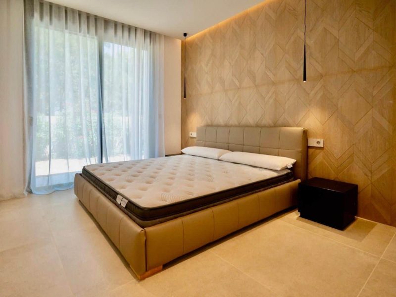 Bedroom with a panelled headboard wall and a sliding door onto the terrace