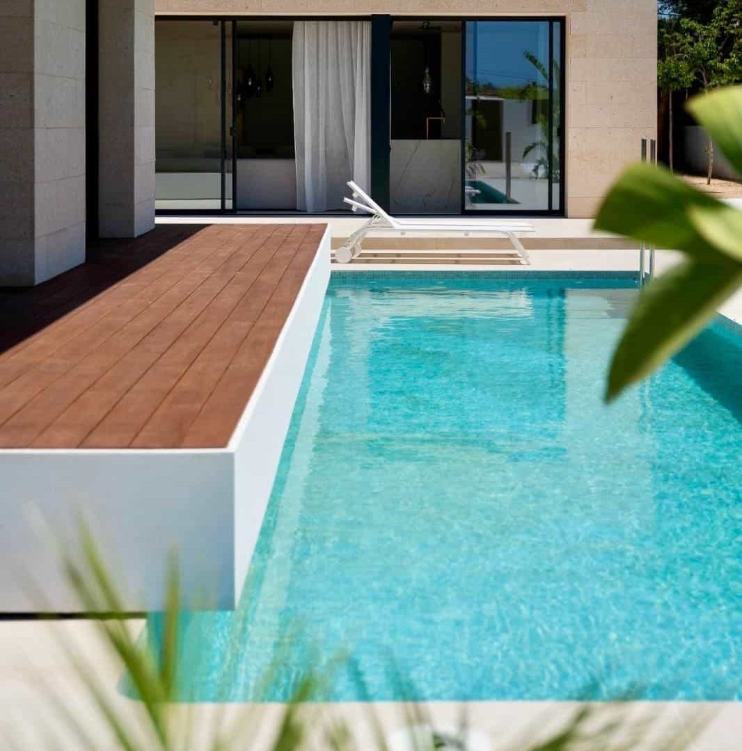 The pool seen past palm leaves, with the villa's glass doors behind